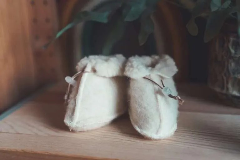 Baby draagt crèmekleurige wollen slofjes